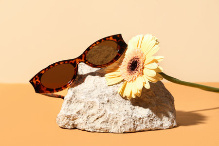 Stone with stylish sunglasses and beautiful gerbera flower on colorful backgroundの写真素材