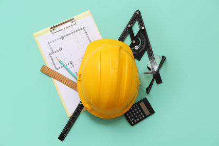 Architect's supplies with hardhat and house plan on green background