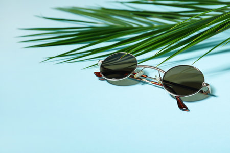 Stylish sunglasses and palm leaf on blue backgroundの写真素材
