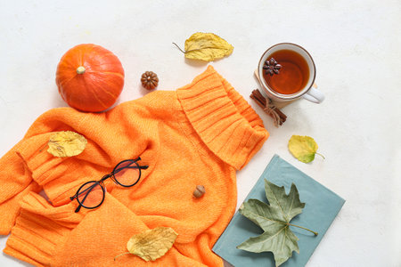 Composition with stylish warm sweater, book, cup of tea and autumn decor on light backgroundの写真素材