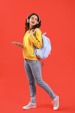 Female student in headphones with tablet computer on red backgroundの写真素材