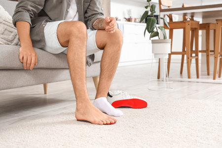 Young man with flat feet fitting orthopedic insole at home, closeupの写真素材