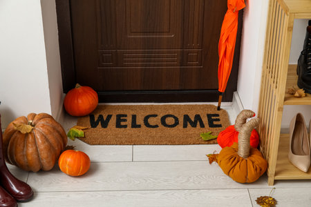 Door mat with female shoes, umbrella and autumn decor in hallwayの写真素材