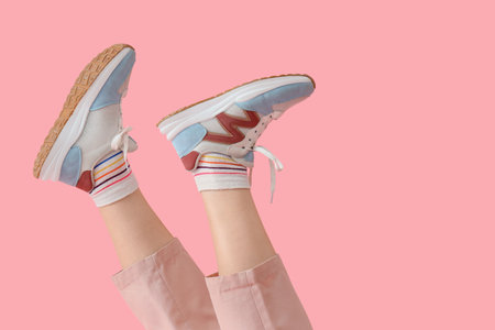 Female legs in sneakers and trousers on pink backgroundの写真素材