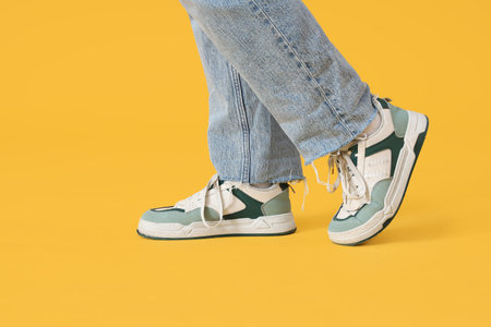 Female legs in stylish sneakers and jeans on yellow backgroundの写真素材