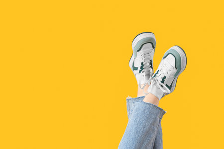 Female legs in stylish sneakers and jeans on yellow backgroundの写真素材