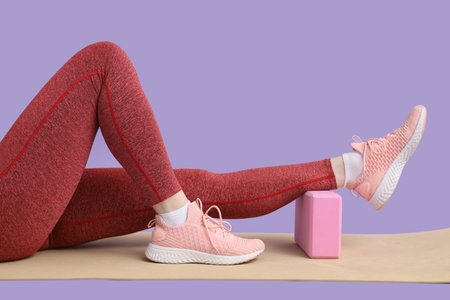 Female legs in sneakers with yoga block on mat on lilac backgroundの写真素材