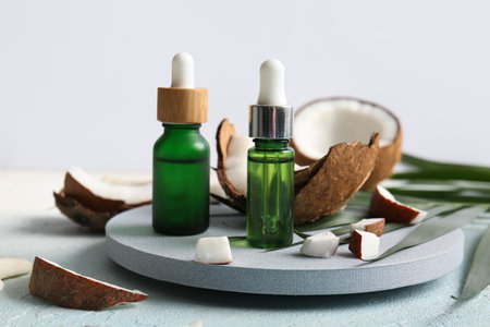 Decorative podium with bottles of coconut cosmetic oil and palm leaf on light blue tableの写真素材