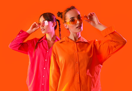 Beautiful young fashionable sisters in stylish outfits on orange background