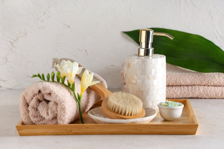 Wooden board with spa accessories and freesia flower on light background