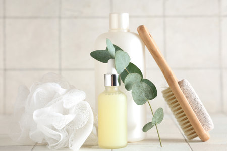 Bottles of cosmetic products, massage brush and bath sponge on light tile backgroundの写真素材