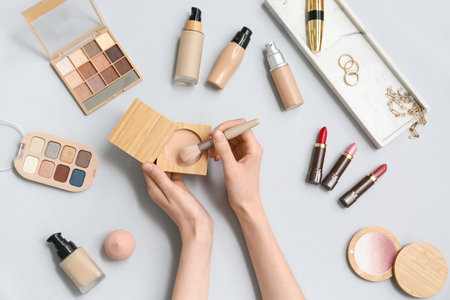 Female hands with makeup powder, brush and different cosmetic products on gray backgroundの写真素材