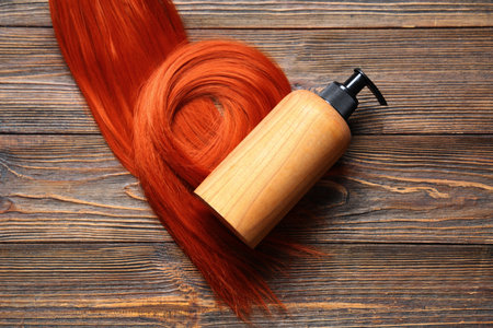 Bottle of cosmetic product and red hair strand on wooden backgroundの写真素材