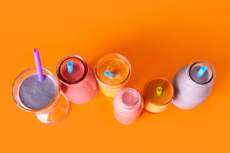 Glasses and bottles of different fresh smoothie on orange background