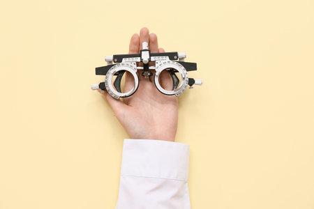 Doctor hand with optical trial frame on yellow background