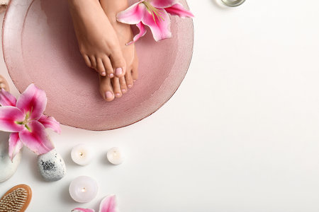 Female legs in bowl for spa procedure with water, orchid flowers and candles on white backgroundの写真素材