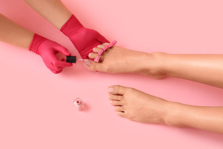 Young woman getting pedicure with nail polish on pink backgroundの写真素材