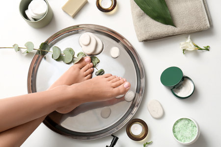Female legs in bowl for spa procedure with stones, eucalyptus and bath items on white backgroundの写真素材
