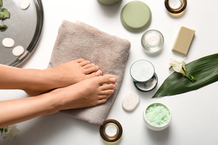 Female legs with towel, candles and bath items for spa procedure on white backgroundの写真素材