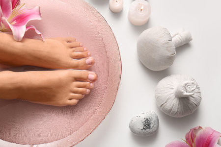 Female legs in bowl for spa procedure with water, orchid flower and bath items on white backgroundの写真素材