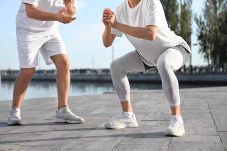 Sporty young woman exercising with personal trainer outdoors, closeup