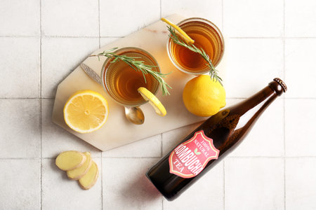 Bottle and glasses of tasty kombucha tea with lemon and ginger on white tile backgroundの写真素材
