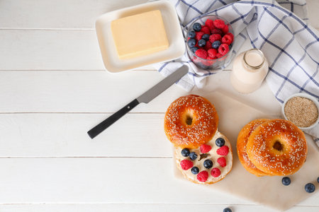 Board of tasty bagels with berries and butter on white wooden backgroundの写真素材