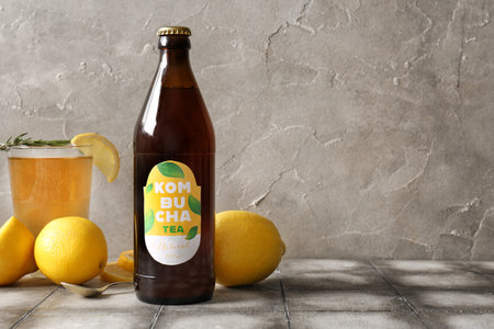 Bottle and glass of tasty kombucha tea with lemon on gray tile table