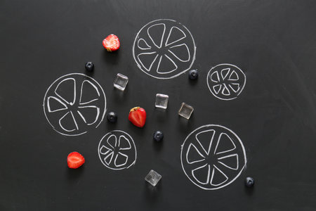 Berries, ice cubes and drawn sliced citrus fruits on black backgroundの写真素材