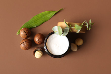 Macadamia nuts, green leaves and jar of cosmetic product on brown background, closeupの写真素材