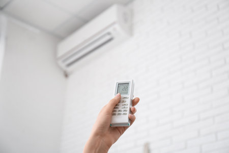 Female hand with air conditioner remote control at home, closeupの写真素材