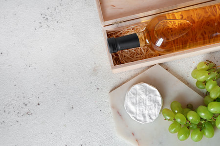 Box with bottle of wine, glasses, grapes and Camembert cheese on white grunge backgroundの写真素材