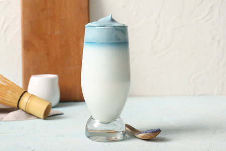 Glass of blue dalgona matcha latte and wooden spoon with powdered matcha on light tableの写真素材