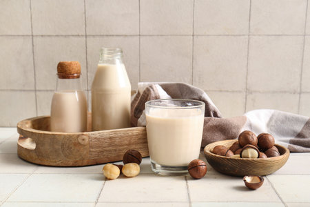 Glass and bottles of fresh macadamia milk on white tile backgroundの写真素材