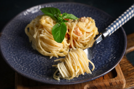 Dark plate and fork with tasty pasta carbonara on wooden tray as background, closeupの写真素材