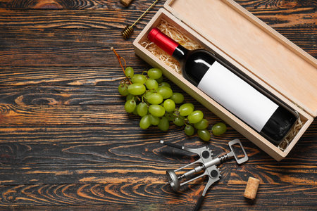 Box with bottle of wine, grapes and corkscrew on brown wooden backgroundの写真素材