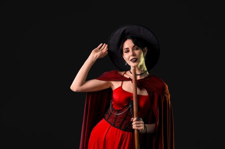 Beautiful young woman dressed as witch for Halloween with broom on black backgroundの写真素材