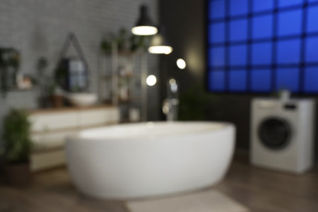 Blurred view of dark bathroom with bathtub, washing machine and glowing lamps in eveningの写真素材