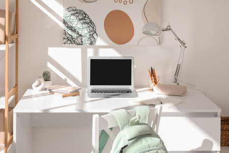 Modern school desk with stationery and laptop in room near white wallの写真素材