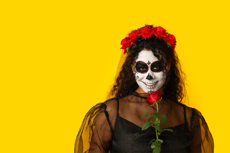 Young African-American woman dressed for Halloween with rose on yellow background