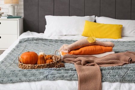 Sweaters with pumpkins and autumn leaves on bed in roomの写真素材