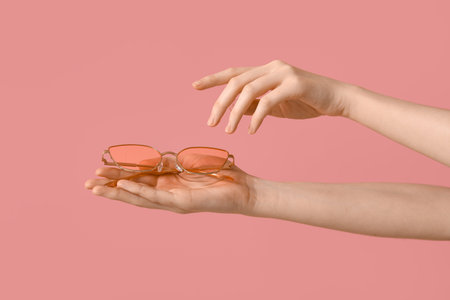 Female hands with stylish sunglasses on pink background