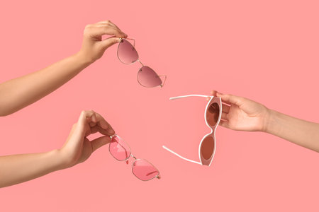 Female hands with different stylish sunglasses on pink backgroundの写真素材