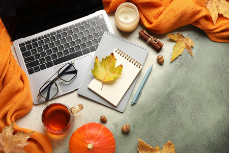 Composition with modern laptop, notebooks, cup of tea and autumn decor on grunge background