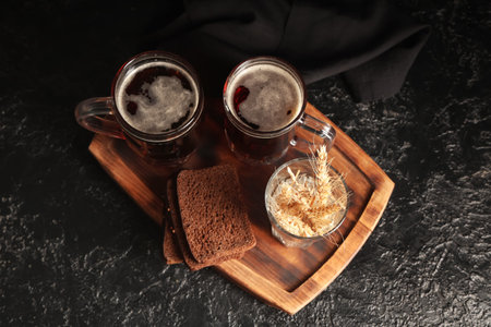 Glasses of fresh kvass with slices of bread and wheat on black background