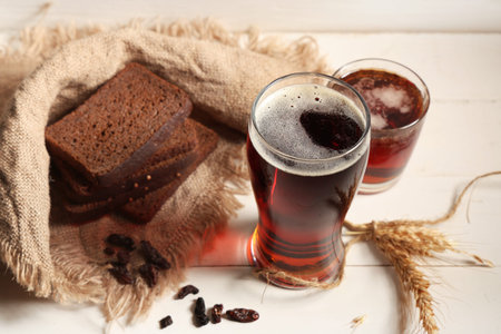 Glasses of fresh kvass with slices of bread and wheat on white wooden background