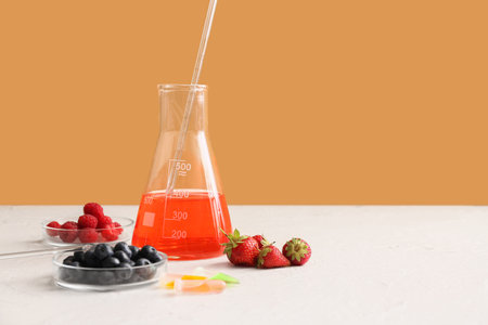 Professional laboratory glassware with sample and berries on table near orange wallの写真素材