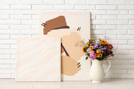 Pictures and vase with wild flowers near white brick wall in roomの写真素材
