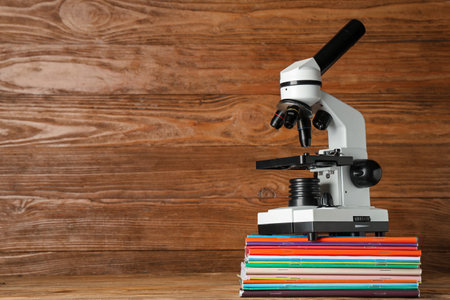 Modern microscope with copybooks on table against wooden backgroundの写真素材