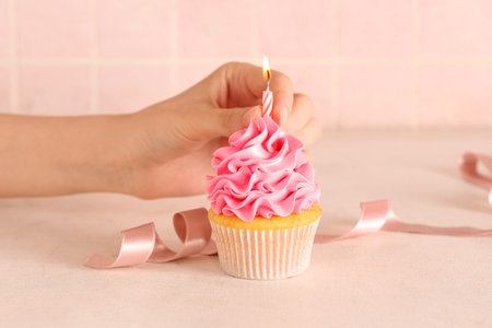 Female hand and sweet Birthday cupcake with burning candle on white table